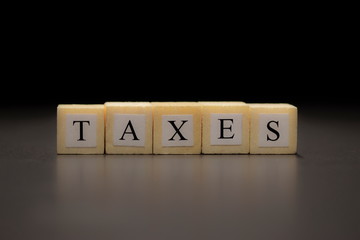 The word TAXES written on  wooden cubes isolated on a black background