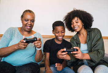 Grandmother, mother and son playing video games at home.