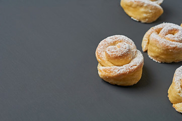 Scattered homemade baked buns in form of rose spangled of powdered sugar lies on dark concrete desk. Confectioners workplace. Space for text