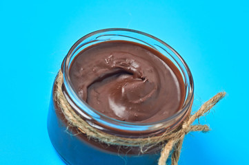 Single glass transparent jar with rope full of melted chocolate or cream lies on blue desk on kitchen. Concept of nutritious breakfast or lunch. Close-up