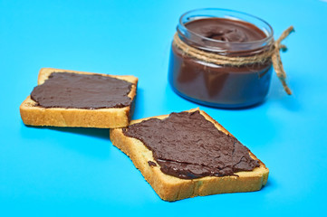 Single glass transparent jar with rope full of melted chocolate or cream near pieces of vanilla bread lies on blue desk on kitchen. Concept of nutritious breakfast or lunch