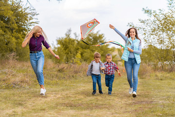 Happy non traditional family of two young mother and their kids launch a kite on nature at sunset