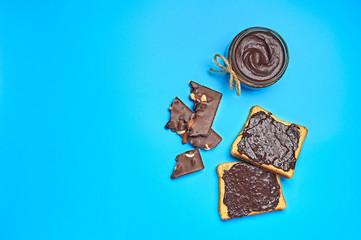 Single glass transparent jar with rope full of melted chocolate or cream near two pieces of vanilla bread lies on blue desk on kitchen. Concept of nutritious breakfast or lunch
