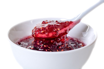 White ceramic spoon and bowl of blackberry jam on white background