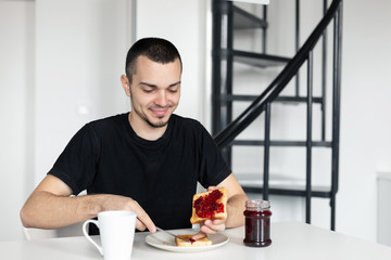 The guy has breakfast with toast with jam.