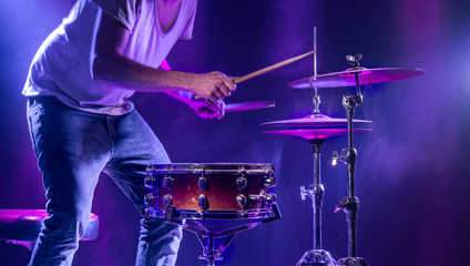 Naklejka premium A drummer plays drums on a blue background. Beautiful special effects of light and smoke. The process of playing a musical instrument.