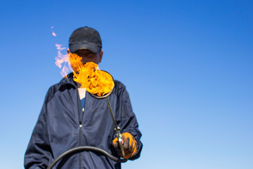 a burner with a fire on a blurred background of a working roofer in dirty clothes