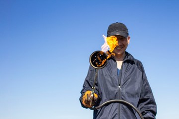 a burner with a fire on a blurred background of a working roofer in dirty clothes