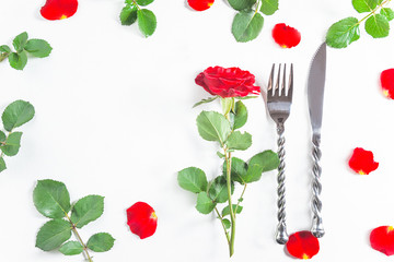 Romantic table setting for Valentine's day dinner. Beautiful cutlery, one red rose and petals on white background. Space for text