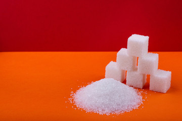 Cubes of white sugar and granulated sugar on an orange background