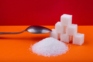 Spoon and cubes of white sugar and granulated sugar on an orange background