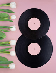 Figure eight made with vintage vinyl records and white tulips on pink background.