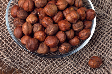 Hazelnuts in a glass plate close-up on burlap and wooden background