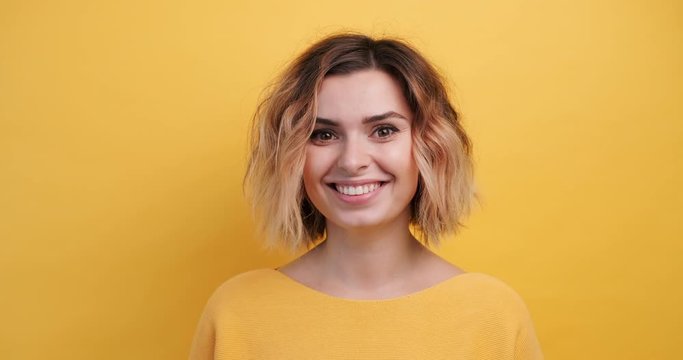 Portrait happy young woman thinks, finding solution Idea pointing forward an index finger on isolated yellow background, looking directly at the camera smiling. Monotone. Emotions of people