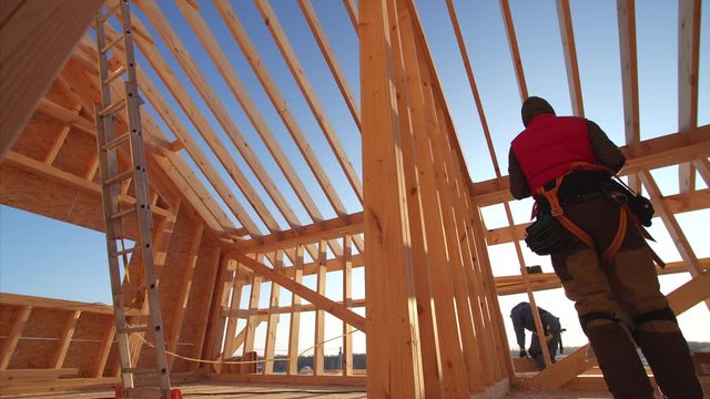 Sliding view from below of worker carrying bag with insulator at frame house building. Blue sky is on the background. Beautiful natural light, sunny day