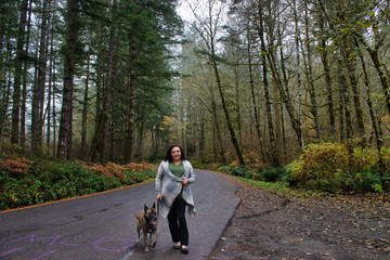 Fototapeta premium ethnic middle aged woman walking large dog in foggy forest