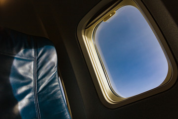 An empty leather chair in air plane. Blue seat beside window with blue sky in flying airplane.