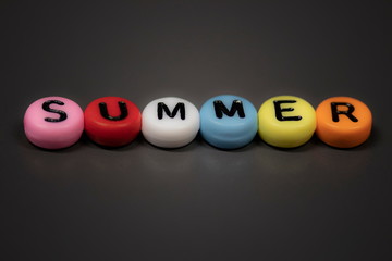 The word SUMMER written with colorful bead letters lying on a table