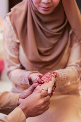 The groom is dressing the ring to the bride's hand during the Malay wedding ceremony in Malaysia. The bride’s hand with henna.