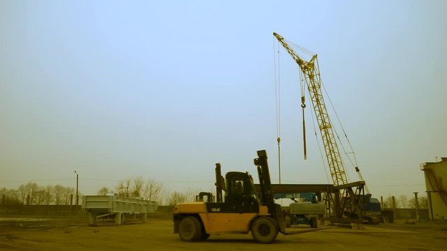 ower crane and loader work against the blue sky. Evening work. Overtime work.
