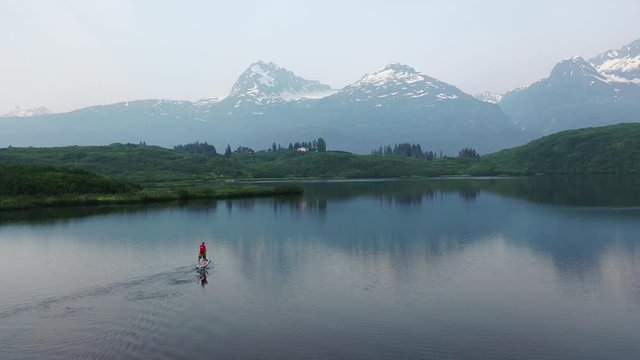 fly in and zoom following behind a paddle boarder on a lake with background mountains.