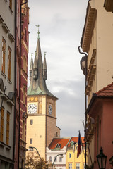 Typical narrow street of Stare Mesto, the historical center of Prague, Czech Republic, with a focus on the belfry and the clock tower of a medieval baroque church