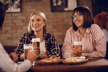 Happy female friends drinking beer while talking in a pub.