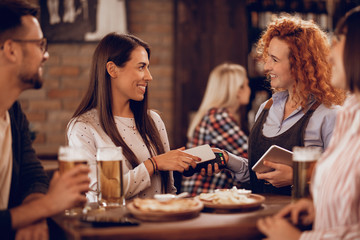 Happy woman paying contactless with smart phone in a bar.