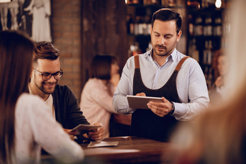 Young waiter using digital tablet while serving guests in a pub.