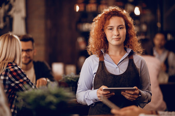 Portrait of young redhead waitress with touchpad in a bar.