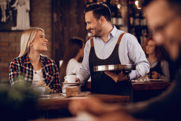 Happy waiter talking to a woman while giving her coffee in a cafe,