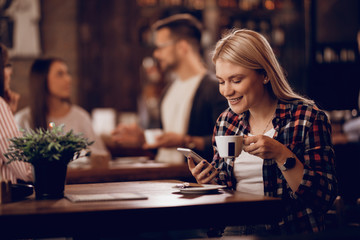 Happy woman using smart phone while drinking coffee in a cafe.