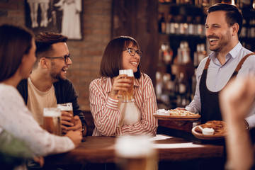 Cheerful waiter serving food to his guests in a pub.