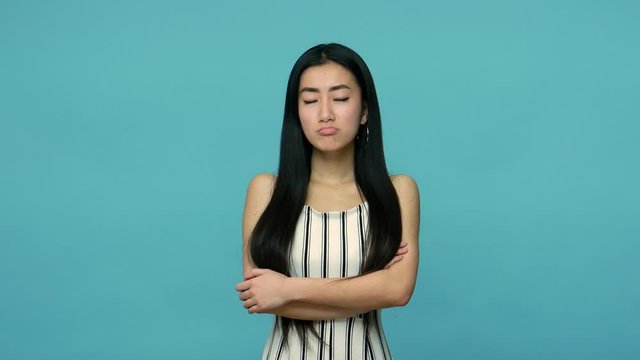 Upset displeased asian woman with long straight black hair in dress crossing hands and looking with resentful vexed expression, feeling unhappy offended. indoor studio shot isolated on blue background