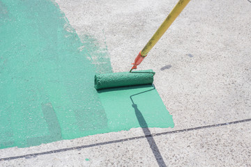 Hand painting a green floor with a paint roller for waterproofing