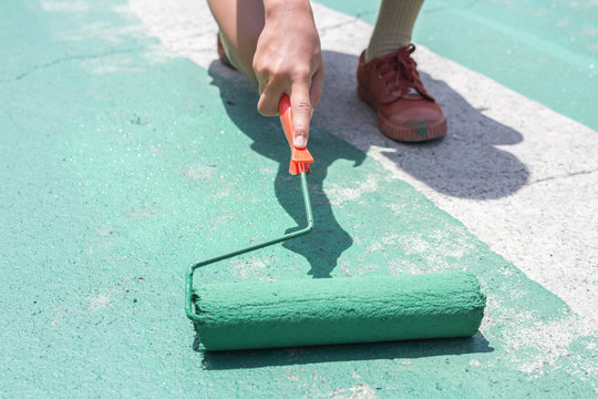 Hand painting a green floor with a paint roller for waterproofing