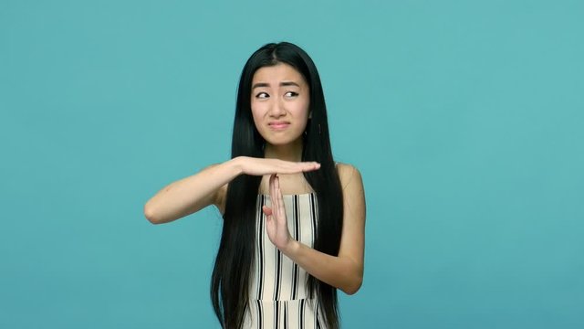 I need more time. Frustrated tired asian woman with long straight black hair making timeout hand gesture, employee asking break with imploring face. indoor studio shot isolated on blue background