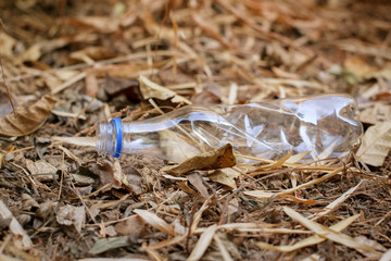 Garbage from plastic bottle that are thrown away on the dry leaves ground with dry leaf which is a problem and pollution to the environment.