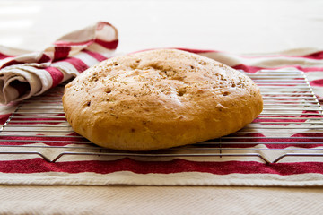 Fresh Focaccia bread with rosemary; Loaf of focaccia bread on a cooling rack with tea towels.