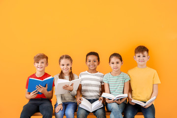 Cute little children reading books on color background