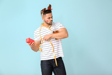 Drunk man with Christmas gift and champagne on color background