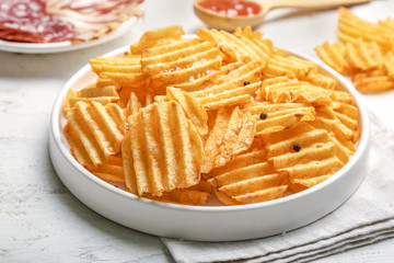 Plate with tasty potato chips on table