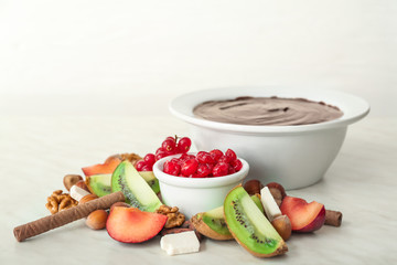 Bowl with tasty chocolate fondue and fruits on table