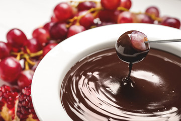 Dipping of tasty grape into bowl with chocolate fondue on table, closeup