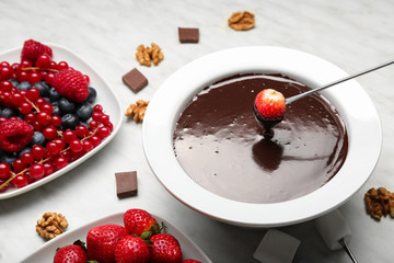 Dipping of tasty strawberry into bowl with chocolate fondue on table