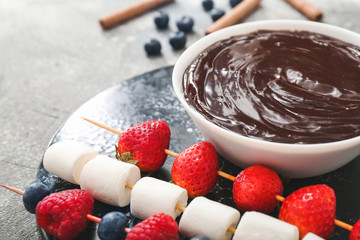 Bowl with tasty chocolate fondue, berries and marshmallow on table
