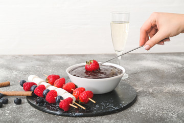 Woman dipping tasty strawberry into bowl with chocolate fondue on table