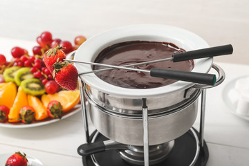 Fondue pot with melted chocolate and strawberry on table