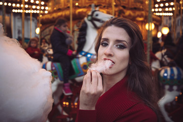 Portrait of a beautiful young girl with white cotton candy in front of a carousel horse