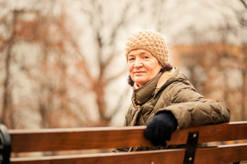 An elderly woman sits on a park bench on an autumn day.